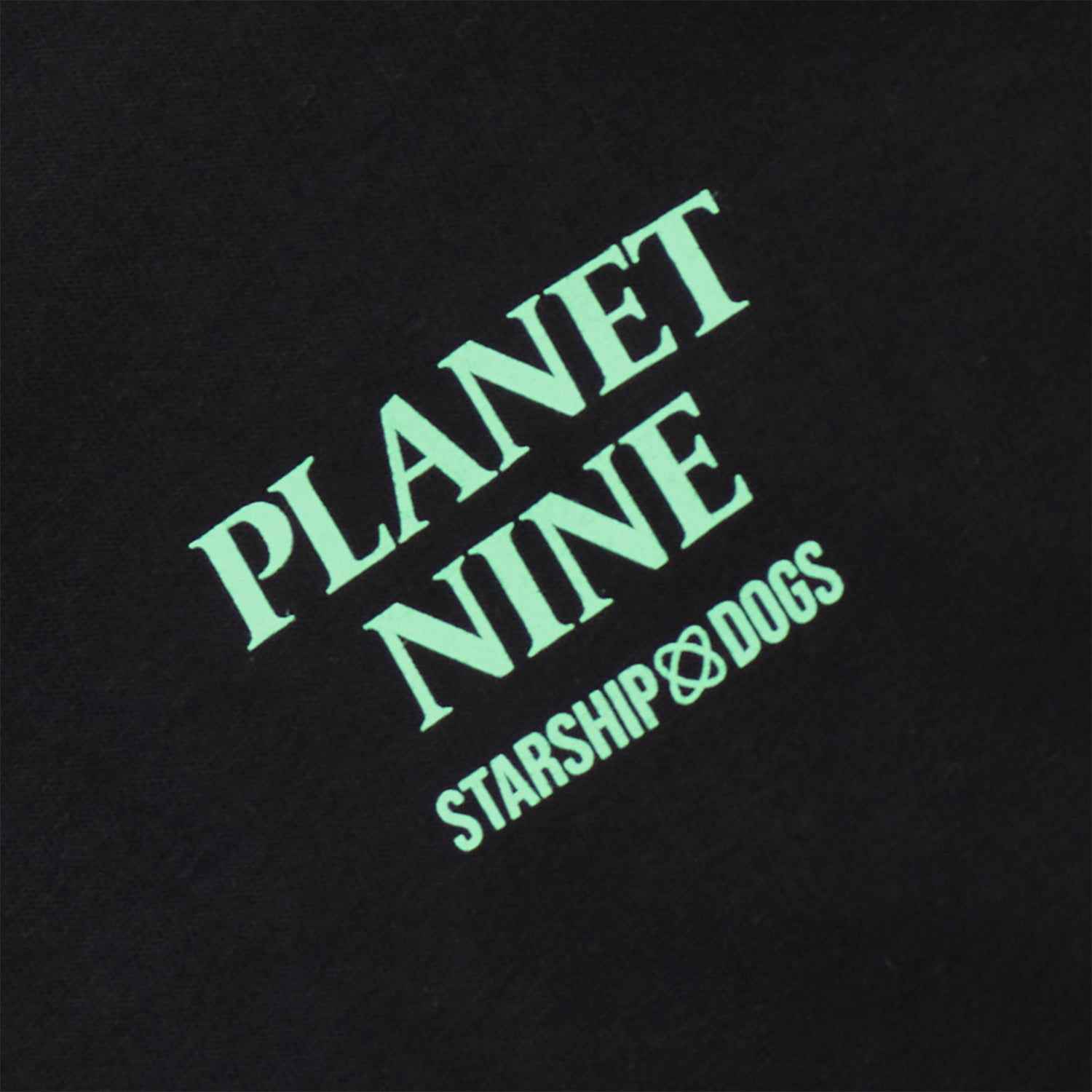 Zoomed-In Photo of the Left Chest Print 'PLANET NINE STARSHIP DOGS'. Body color black. Print color light green.