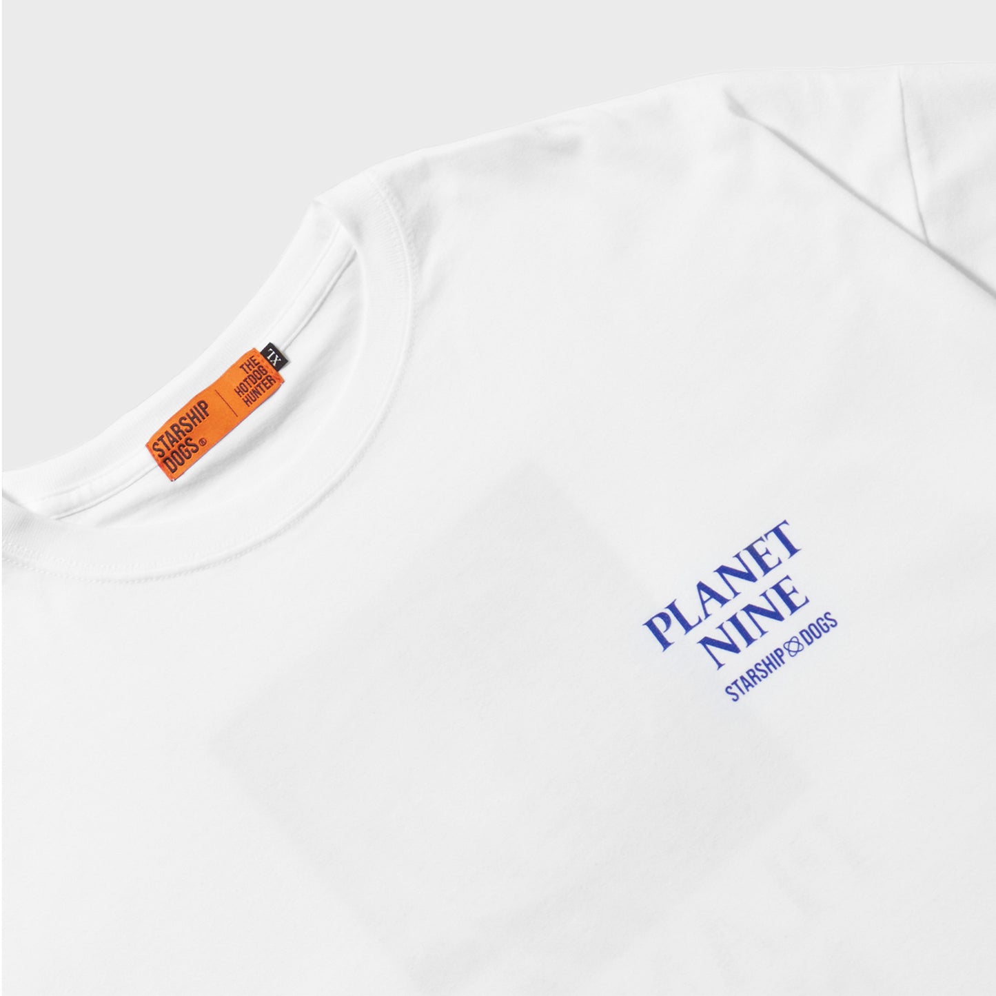 Zoomed-In on the Print Section of the Product: A short-sleeve T-shirt in body color white. On the left chest, 'PLANET NINE STARSHIP DOGS' is written, with the text color in blue. An orange brand tag of STARSHIP DOGS is stitched on the inside of the collar.
