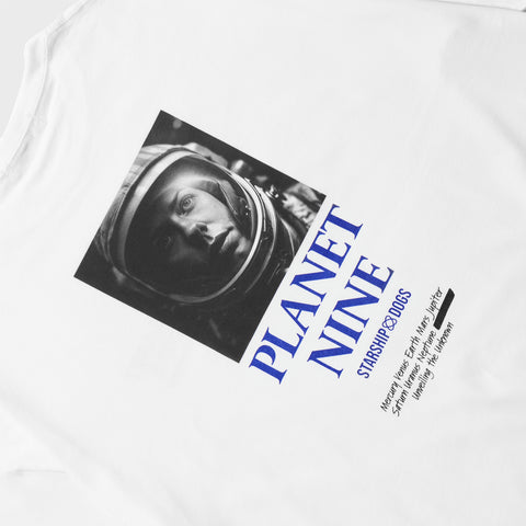 Product Photo: Back print on a white T-shirt. The print showcases a monochrome square photo of a female astronaut's face. Below the photo, the first line reads 'PLANET NINE' in a two-tiered text arrangement. Below that is the brand name 'STARSHIP DOGS.' Further down, in a handwritten-style font, are the names 'Mercury, Venus, Earth, Mars, Jupiter, Saturn, Uranus, Neptune,' followed by another planet name that was previously obscured and blacked out, accompanied by the phrase 'Unveiling the unknown'.
